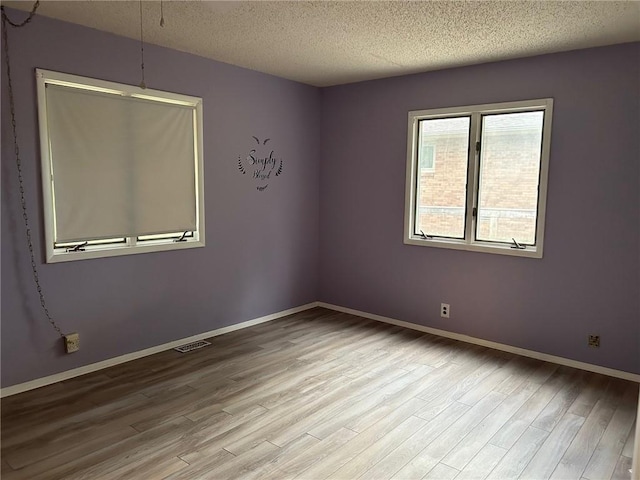 unfurnished room with a textured ceiling and light wood-type flooring