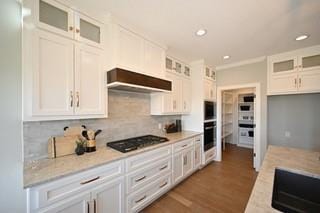 kitchen featuring dark hardwood / wood-style flooring, white cabinetry, black gas cooktop, range hood, and decorative backsplash