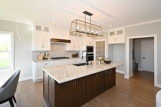 kitchen featuring sink, an island with sink, hanging light fixtures, white cabinetry, and dark wood-type flooring