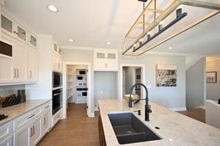 kitchen featuring hanging light fixtures, sink, oven, and white cabinets