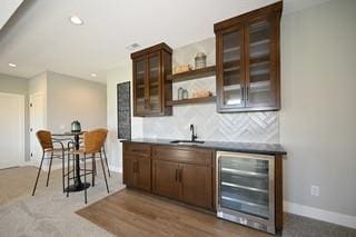 bar featuring dark brown cabinets, decorative backsplash, sink, and beverage cooler