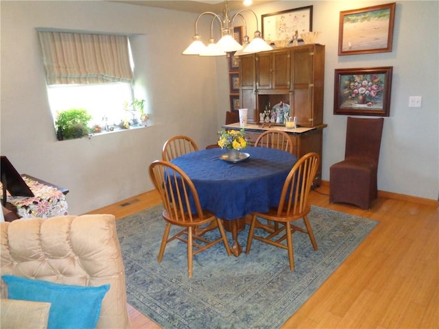 dining area featuring light wood-type flooring, visible vents, a chandelier, and baseboards