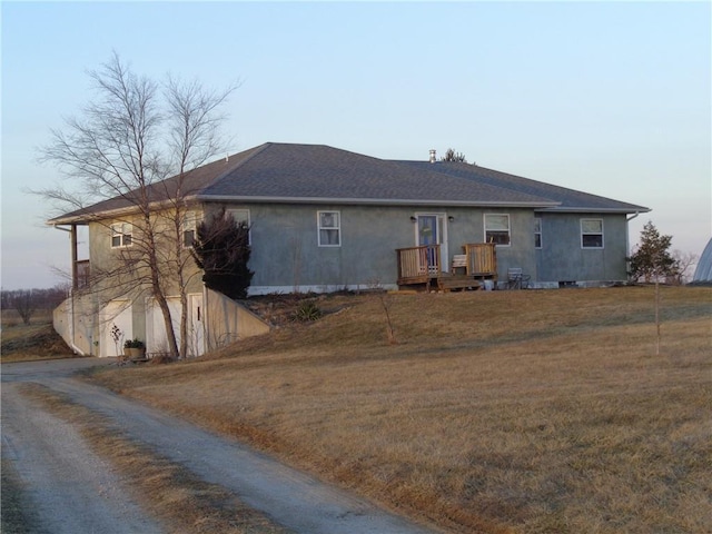 rear view of property featuring gravel driveway, stucco siding, and a yard