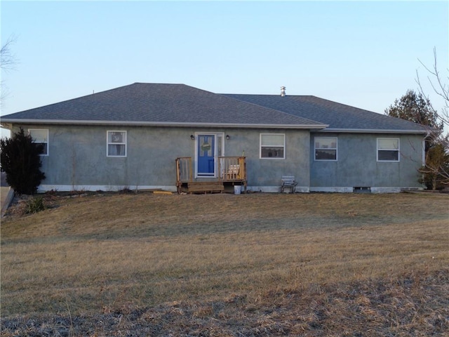 rear view of house with stucco siding, roof with shingles, and a yard