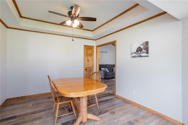 dining room with wood-type flooring, a tray ceiling, ceiling fan, and crown molding