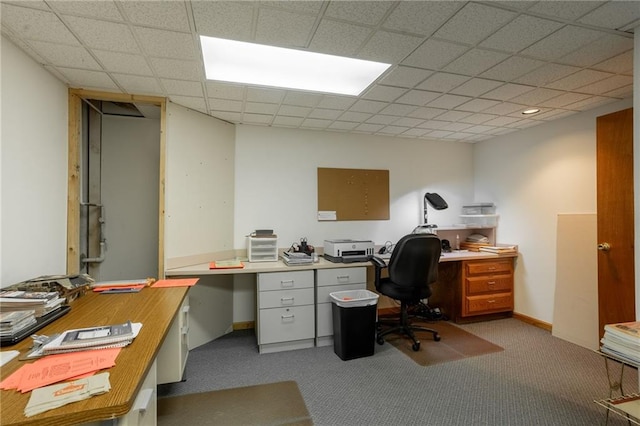 carpeted office with a paneled ceiling and built in desk