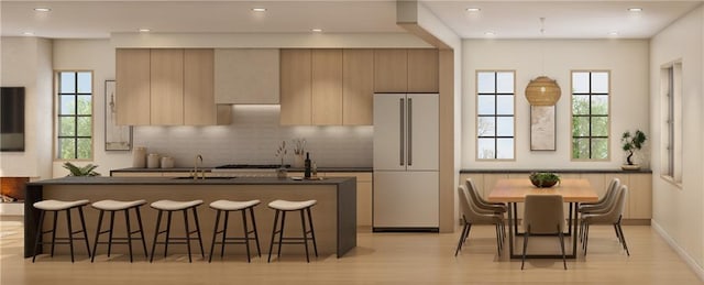 kitchen with tasteful backsplash, an island with sink, sink, white fridge, and light hardwood / wood-style flooring