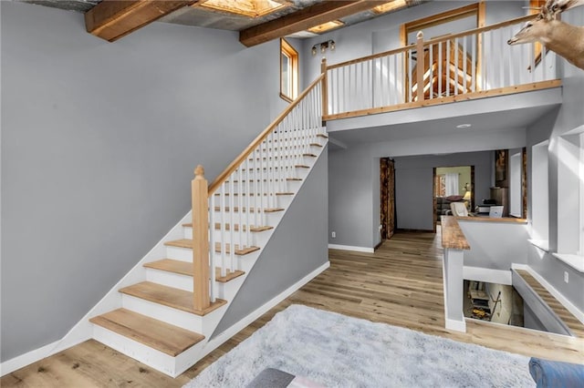 staircase featuring a towering ceiling, beam ceiling, baseboards, and wood finished floors