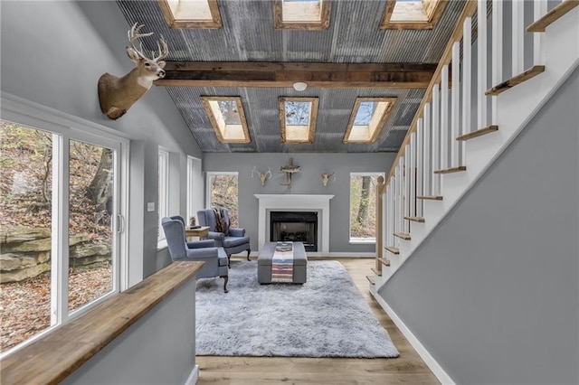 interior space featuring vaulted ceiling with skylight, a fireplace, wood finished floors, baseboards, and stairway