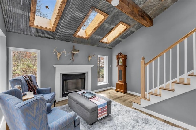 living area with vaulted ceiling with skylight, baseboards, stairway, wood finished floors, and a fireplace