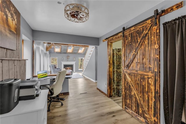 office with a warm lit fireplace, wood finished floors, baseboards, and a barn door