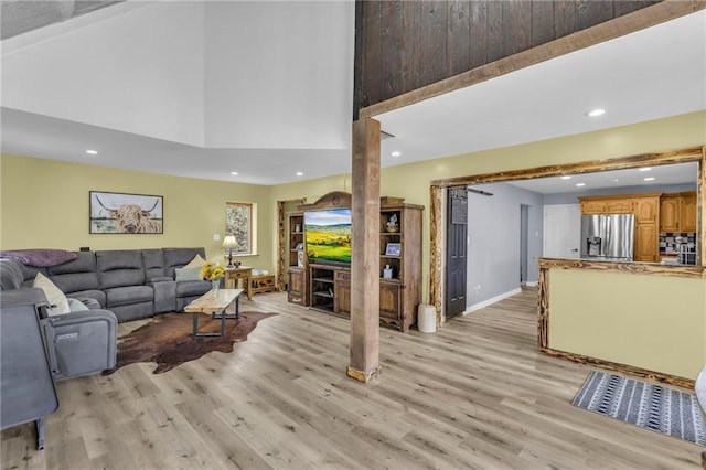 living area with light wood-type flooring, a towering ceiling, baseboards, and recessed lighting