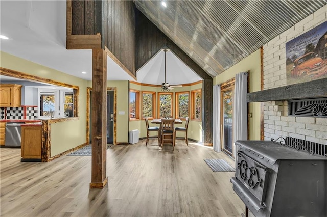 interior space with ceiling fan, high vaulted ceiling, baseboards, light wood-style floors, and a wood stove