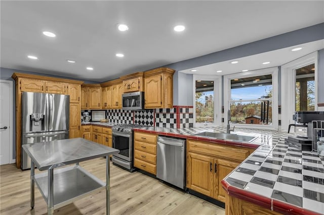 kitchen featuring tile countertops, light wood finished floors, stainless steel appliances, and a sink