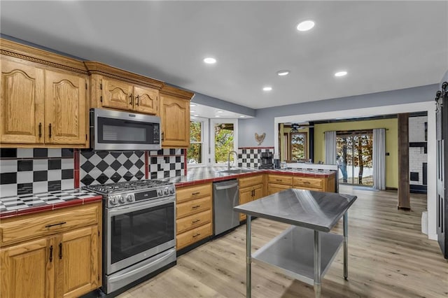 kitchen featuring stainless steel appliances, tile counters, decorative backsplash, a sink, and light wood-type flooring