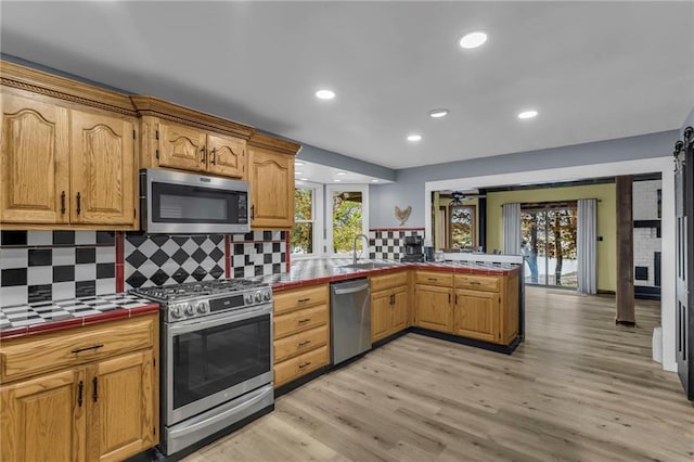 kitchen featuring appliances with stainless steel finishes, light wood-style flooring, tile countertops, and a peninsula