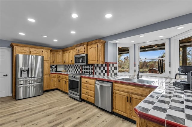 kitchen with appliances with stainless steel finishes, tile counters, light wood-type flooring, and a sink