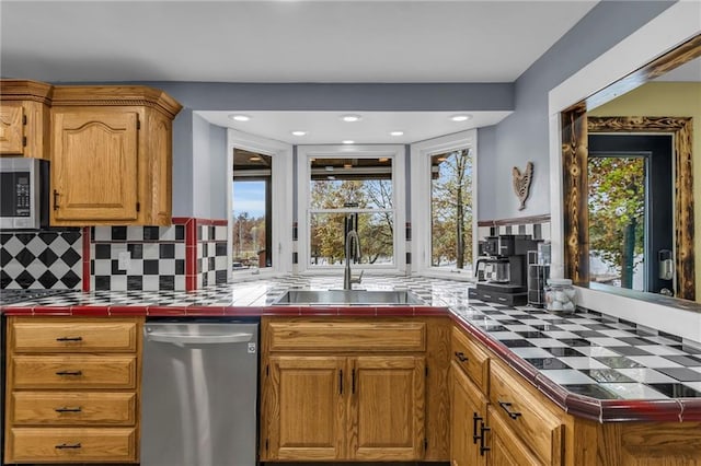 kitchen with tile countertops, stainless steel appliances, backsplash, a healthy amount of sunlight, and a sink