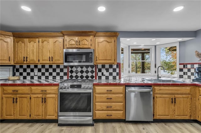 kitchen with appliances with stainless steel finishes, light wood-style floors, a sink, and tile counters