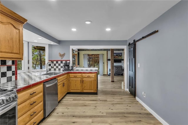 kitchen with a barn door, tile counters, a sink, stainless steel appliances, and backsplash