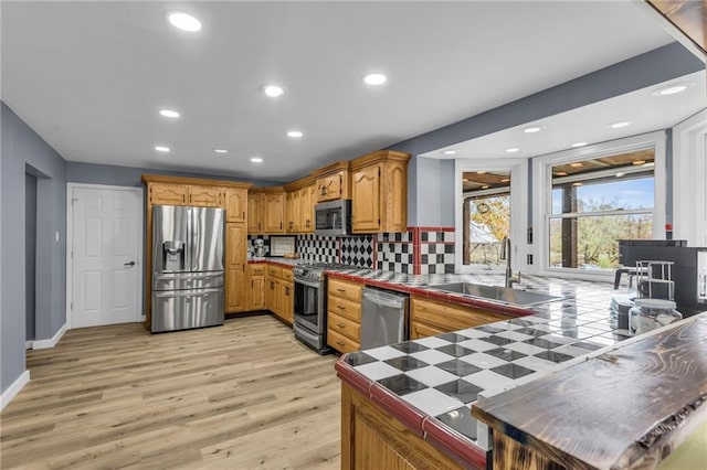 kitchen featuring light wood finished floors, tile countertops, a sink, stainless steel appliances, and backsplash