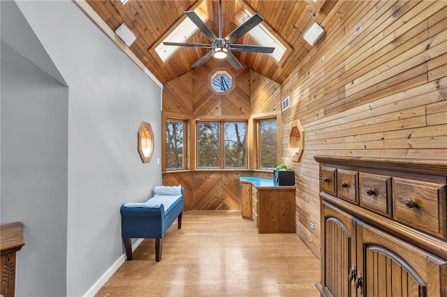 sitting room with high vaulted ceiling, light wood-style flooring, wood walls, a skylight, and a ceiling fan