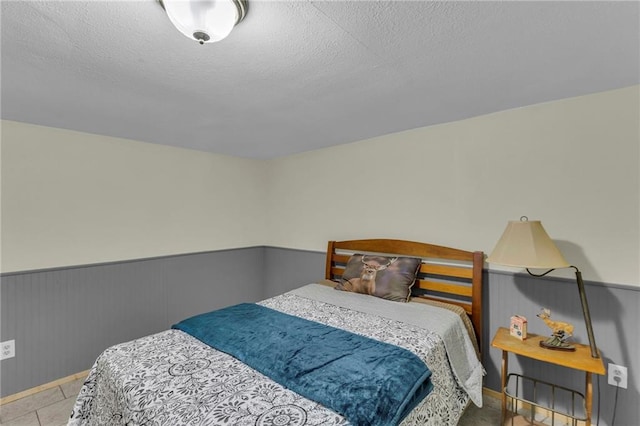 tiled bedroom with a wainscoted wall and a textured ceiling