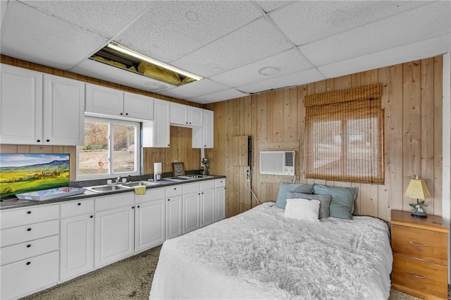 bedroom featuring wooden walls, a drop ceiling, a sink, and light colored carpet