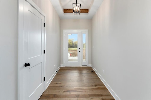 doorway with a tray ceiling, an inviting chandelier, and hardwood / wood-style flooring