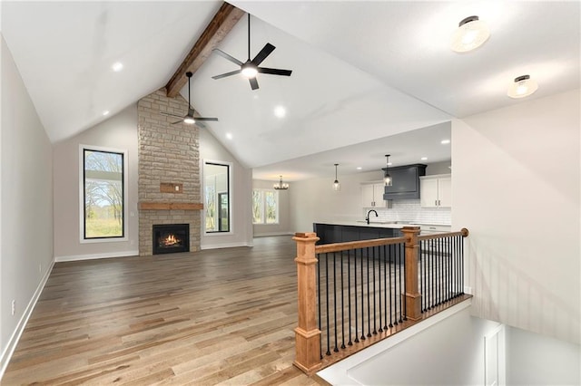 living room featuring a stone fireplace, sink, ceiling fan, beamed ceiling, and light hardwood / wood-style floors