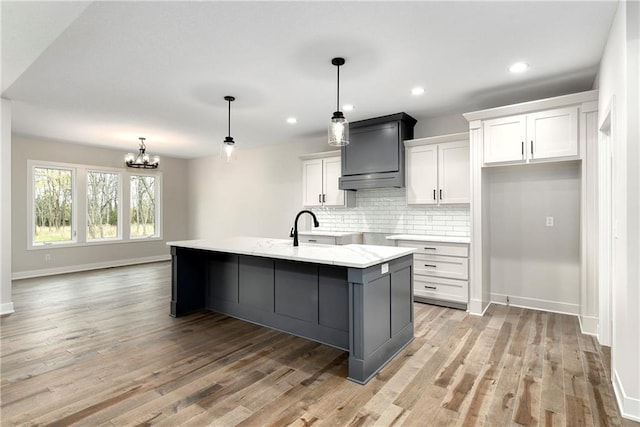 kitchen with white cabinetry, a center island with sink, pendant lighting, and light hardwood / wood-style floors