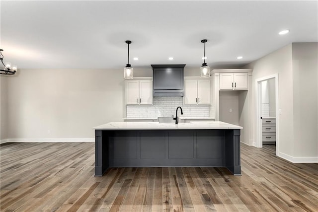 kitchen featuring pendant lighting, hardwood / wood-style flooring, white cabinetry, and an island with sink