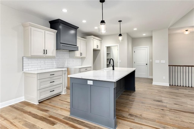 kitchen featuring decorative backsplash, light wood-type flooring, a kitchen island with sink, sink, and pendant lighting