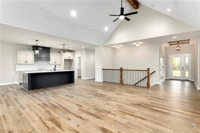 kitchen featuring a center island with sink, white cabinets, sink, hanging light fixtures, and light wood-type flooring