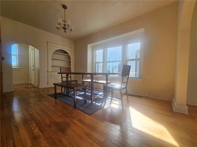 dining room featuring built in shelves, wood-type flooring, a wealth of natural light, and an inviting chandelier