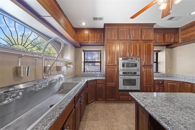 kitchen with light stone counters, ceiling fan, and stainless steel double oven