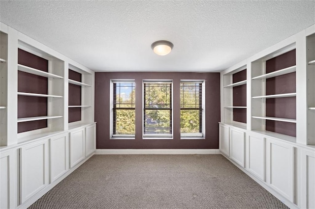 carpeted spare room with built in shelves and a textured ceiling