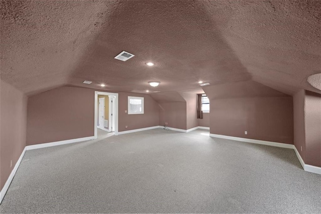 additional living space with vaulted ceiling, carpet, and a textured ceiling