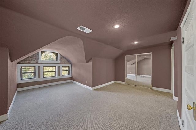 bonus room with vaulted ceiling, light carpet, and a textured ceiling