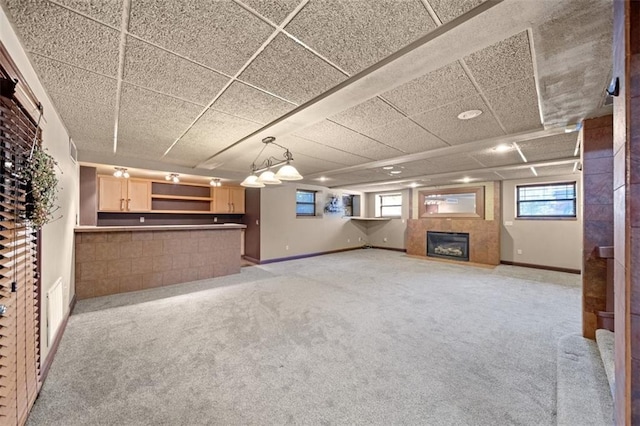 unfurnished living room with a tile fireplace, light colored carpet, and a drop ceiling