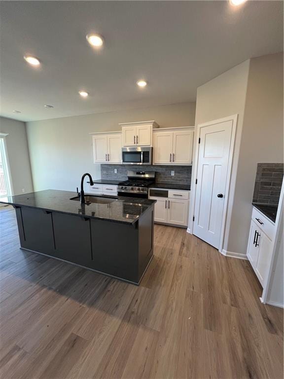 kitchen featuring white cabinetry, sink, stainless steel appliances, wood-type flooring, and a kitchen island with sink