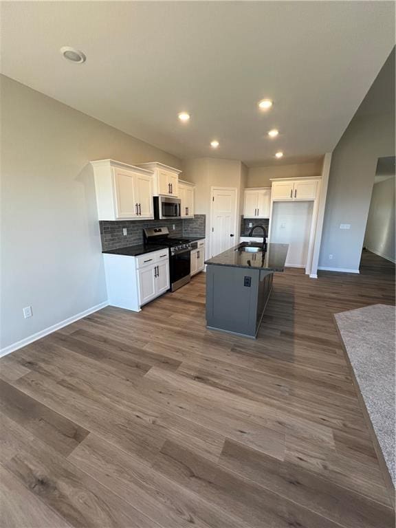 kitchen with appliances with stainless steel finishes, dark hardwood / wood-style flooring, sink, white cabinetry, and an island with sink