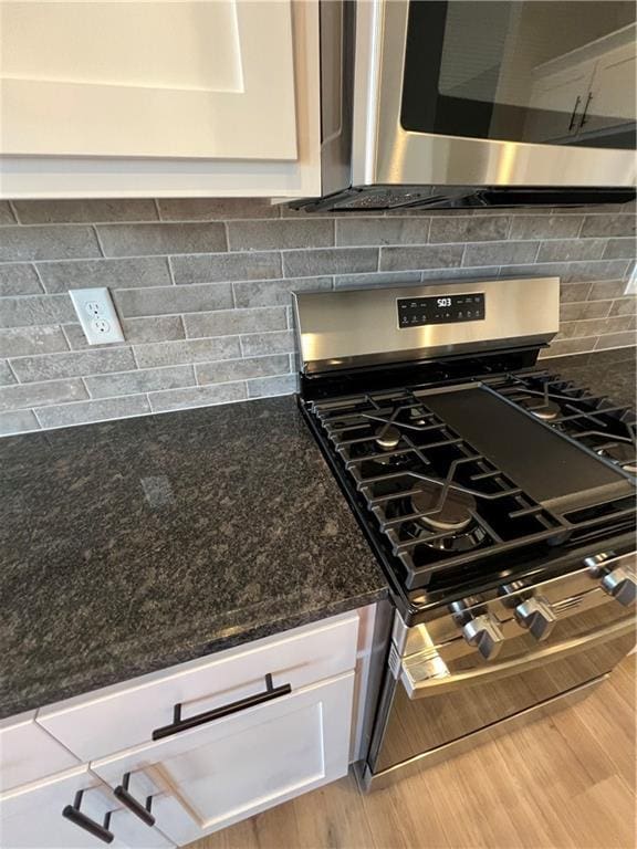 kitchen with stainless steel gas stove, tasteful backsplash, dark stone countertops, white cabinets, and hardwood / wood-style flooring