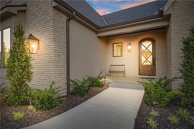 21396 W 93rd Ct, Lenexa, KS 66220 - exterior entry at dusk featuring roof with shingles, brick siding, and stucco siding