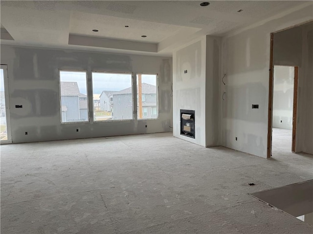 unfurnished living room featuring a tray ceiling and a glass covered fireplace