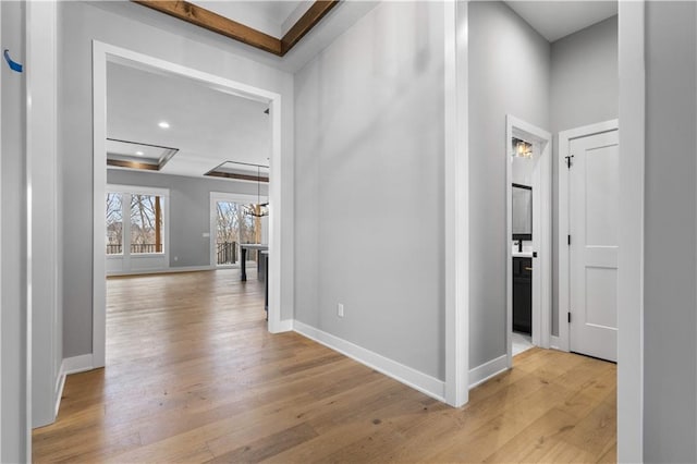 hall with a tray ceiling, light wood-type flooring, and baseboards