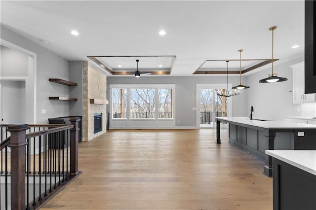 kitchen featuring a tray ceiling, light wood finished floors, light countertops, hanging light fixtures, and open floor plan