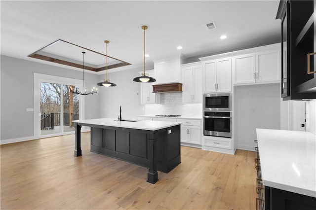 kitchen with an island with sink, appliances with stainless steel finishes, light countertops, and a raised ceiling