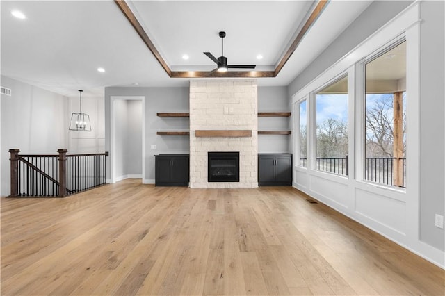 unfurnished living room featuring recessed lighting, a fireplace, visible vents, light wood finished floors, and a raised ceiling