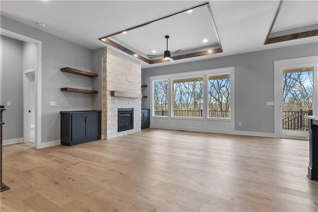 unfurnished living room with a fireplace, a raised ceiling, light wood-style flooring, a ceiling fan, and baseboards